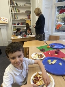 Year 2 pupils cutting pieces of colourful fruit for a fruit salad.